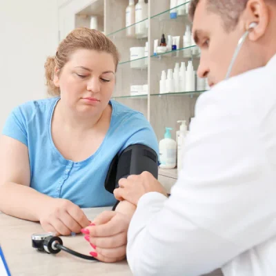 A clinician taking a woman's blood pressure using a cuff and stethoscope in a clinic.